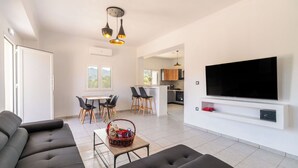 A modern living room with a sofa, a TV, and a dining area with chairs and a table.