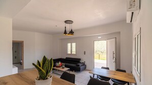 A modern living area with a sofa, dining table, chairs, a potted plant, and a ceiling light fixture.