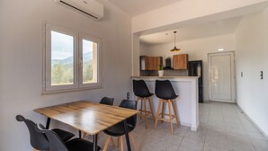 A compact kitchen with a central island, two black chairs, a wooden dining table, and a view through a window.