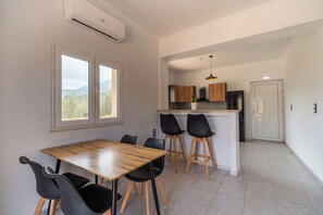 Eine kleine Küche mit einer zentralen Kochinsel, zwei schwarzen Stühlen, einem Holztisch und Blick durch ein Fenster.