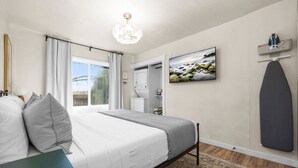 Ein Schlafzimmer mit Bett, Nachttisch, Kommode, Spiegel, Fernseher und Duschbereich.