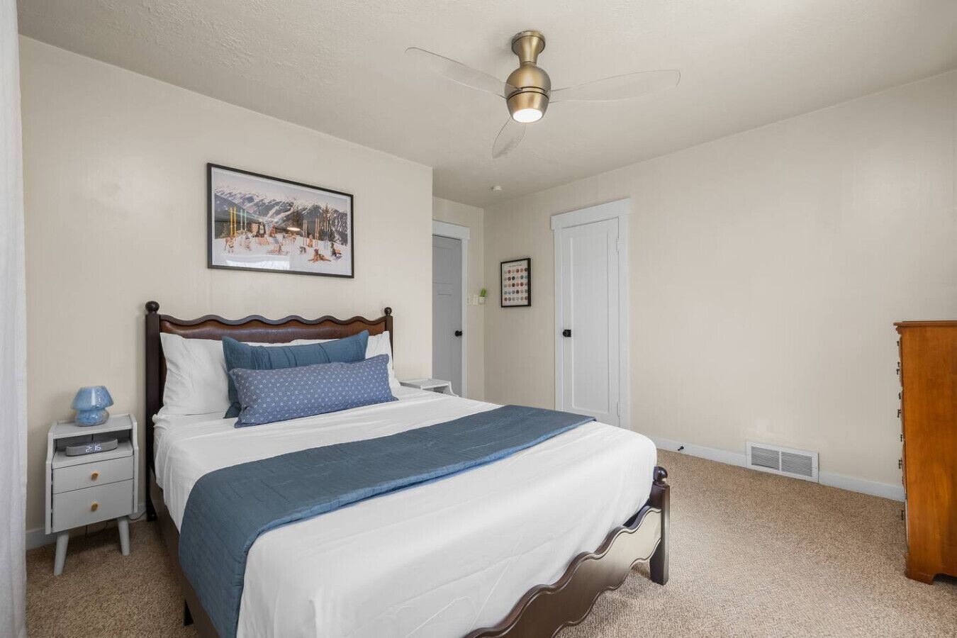 A bedroom with a bed, a nightstand, a ceiling fan, a door, and a wooden dresser.