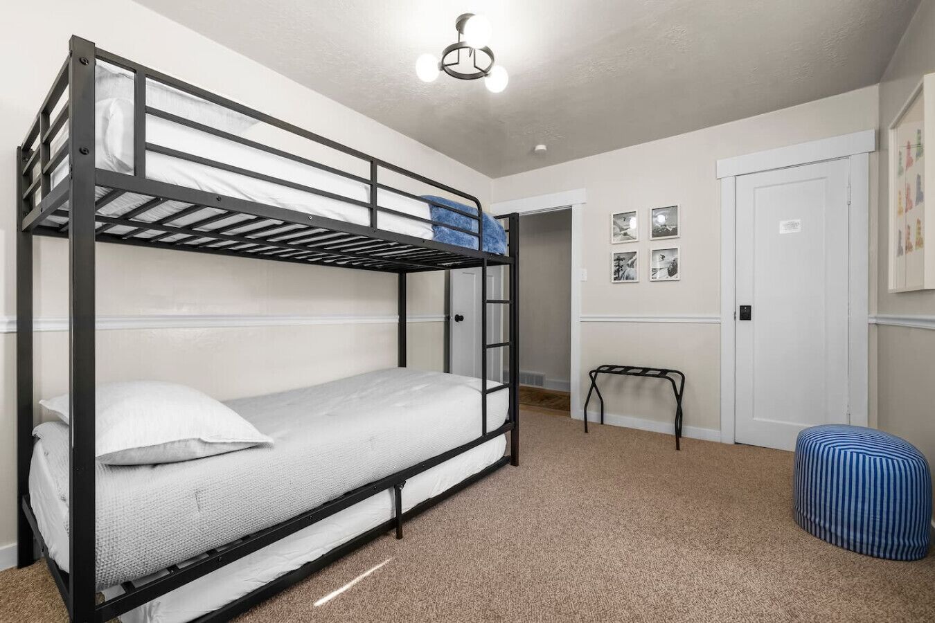 Habitación con literas, una mesita pequeña, un reposapiés, una puerta y una lámpara.