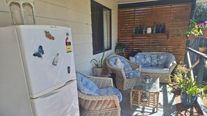 Un patio techado al aire libre con mobiliario de mimbre, un refrigerador con imanes y plantas en macetas.