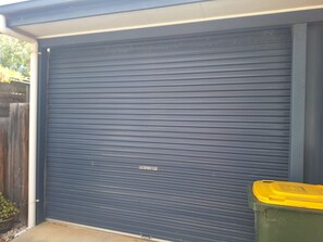 Portone del garage chiuso con un bidone della spazzatura verde accanto.