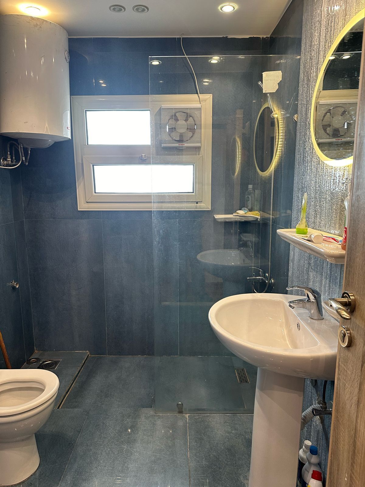 A bathroom with a toilet, sink, shower, and a window.