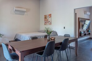 A modern room with a wooden dining table, two chairs, a small plant, a bed with a patterned bedspread, and a wall-mounted air conditioner. - Beautiful Spacious Apartment in the Heart of Santa Theresa (Santa Teresa)