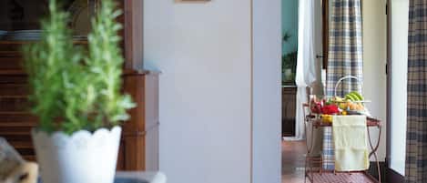 A hallway with a potted plant, a metal cart with fruits and a vase, and a door leading to another room.