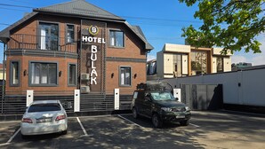 Ett hotell som heter ”Hotel Bulak” med en fasad av tegel, stora fönster och en parkeringsplats med plats för två bilar.