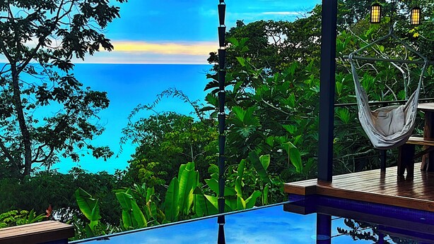 An infinity pool with a wooden deck, a hammock, and lush greenery. - Stunning Ocean View House with Pool, Outdoor Kitchen, and Rancho (Savegre de Aguirre)