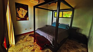 A four-poster bed with a stone floor, a painting on the wall, and a window with a view of greenery. - Stunning Ocean View House with Pool, Outdoor Kitchen, and Rancho (Savegre de Aguirre)