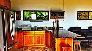 A kitchen with wooden cabinets, a stone floor, a refrigerator, a sink, and a countertop. - Stunning Ocean View House with Pool, Outdoor Kitchen, and Rancho (Savegre de Aguirre)