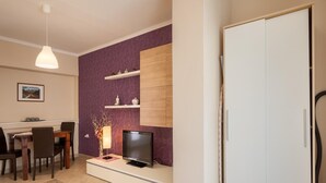 A modern living room with a dining area, a flat-screen TV, a white wardrobe, and a purple accent wall. - Apartment in Porec Near Spadici Beach (Porec)
