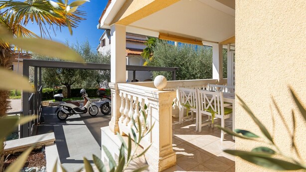 A covered outdoor seating area with a white balustrade, a stone pillar, and a view of a parked scooter and motorcycle. - Apartment in Porec Near Spadici Beach (Porec)