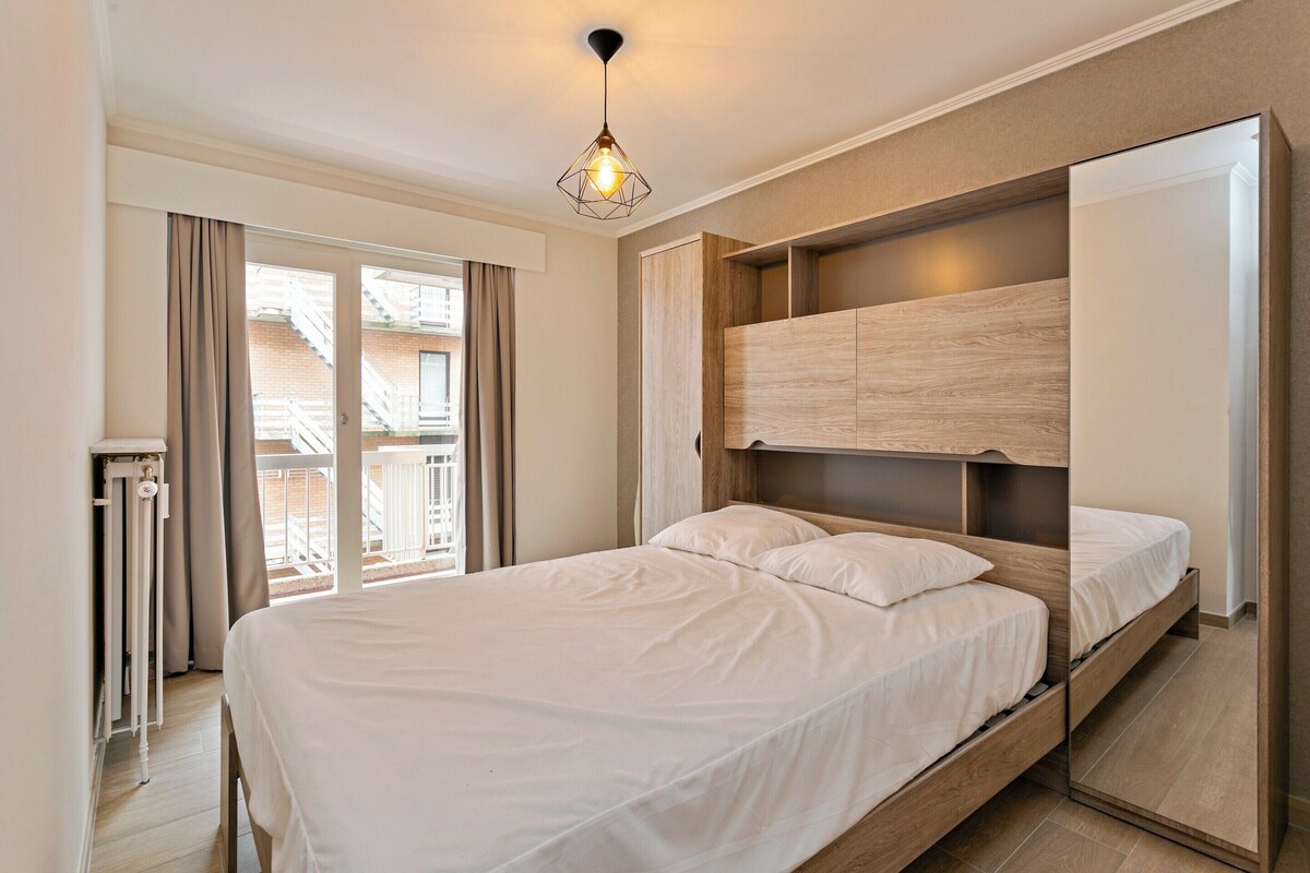 A modern bedroom with a large bed, built-in storage, a view of the outside balcony, and a unique geometric pendant light.
