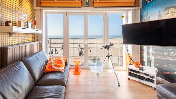 Un salon avec un canapé en cuir, une table basse en verre, un téléviseur et un balcon donnant sur la plage.