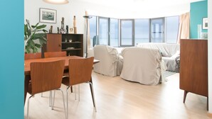 Un salon moderne avec une table à manger en bois, des chaises, un canapé et une grande fenêtre donnant sur la mer.