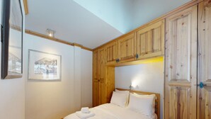 Une chambre avec une armoire en bois, un lit recouvert de draps blancs et un tableau encadré accroché au mur.