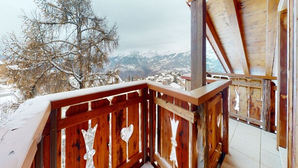 Un balcon en bois offrant une vue sur des montagnes enneigées.
