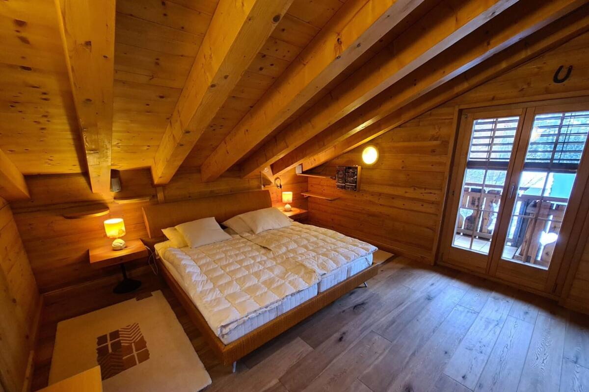 A wooden cabin bedroom with a bed, nightstands, a window, and a sloped ceiling.