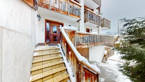 Un immeuble à plusieurs étages, avec un escalier en bois menant à une porte, le tout entouré de neige.