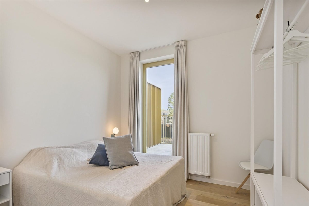 Ein Schlafzimmer mit Bett, Nachttisch, Stuhl und einem Fenster mit Vorhängen.