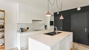 Una cocina moderna con armarios blancos, una isla central, una puerta negra e iluminación colgante.