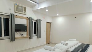 A hotel room with three beds, a large mirror, a window with curtains, a wall-mounted air conditioner, and a wooden door. - Hotel Assi Retreat (Varanasi)