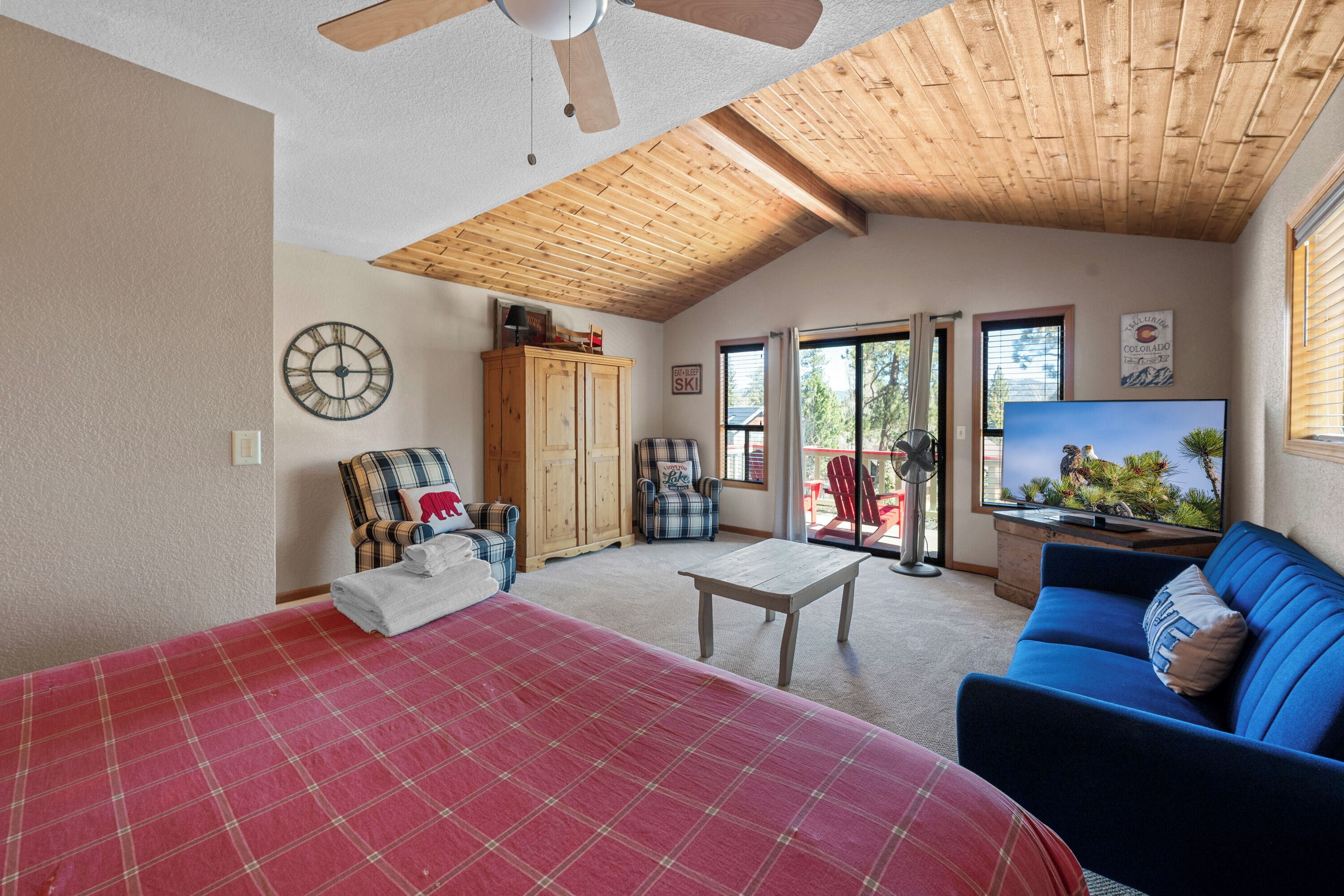 Ein geräumiges Zimmer mit einem großen Bett, einem blauen Sofa, einer Holzbalkendecke und einem Fernseher.