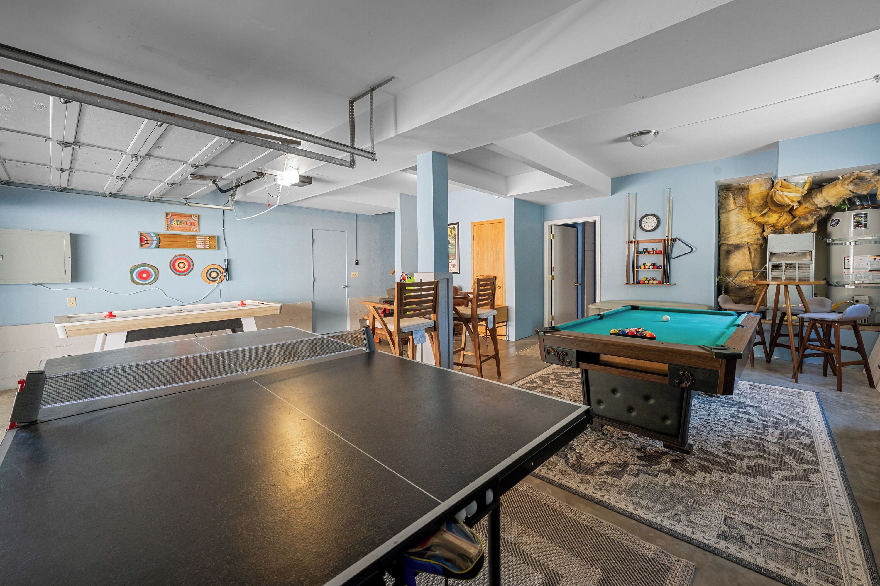 A room with a ping pong table, pool table, and a dartboard.