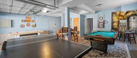 A room with a ping pong table, pool table, and a dartboard.