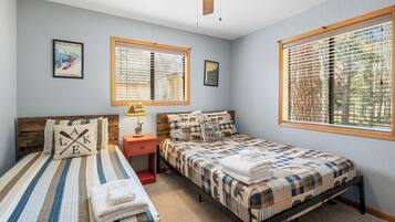 Un dormitorio con dos camas, un ventilador de techo y ventanas amplias con persianas.