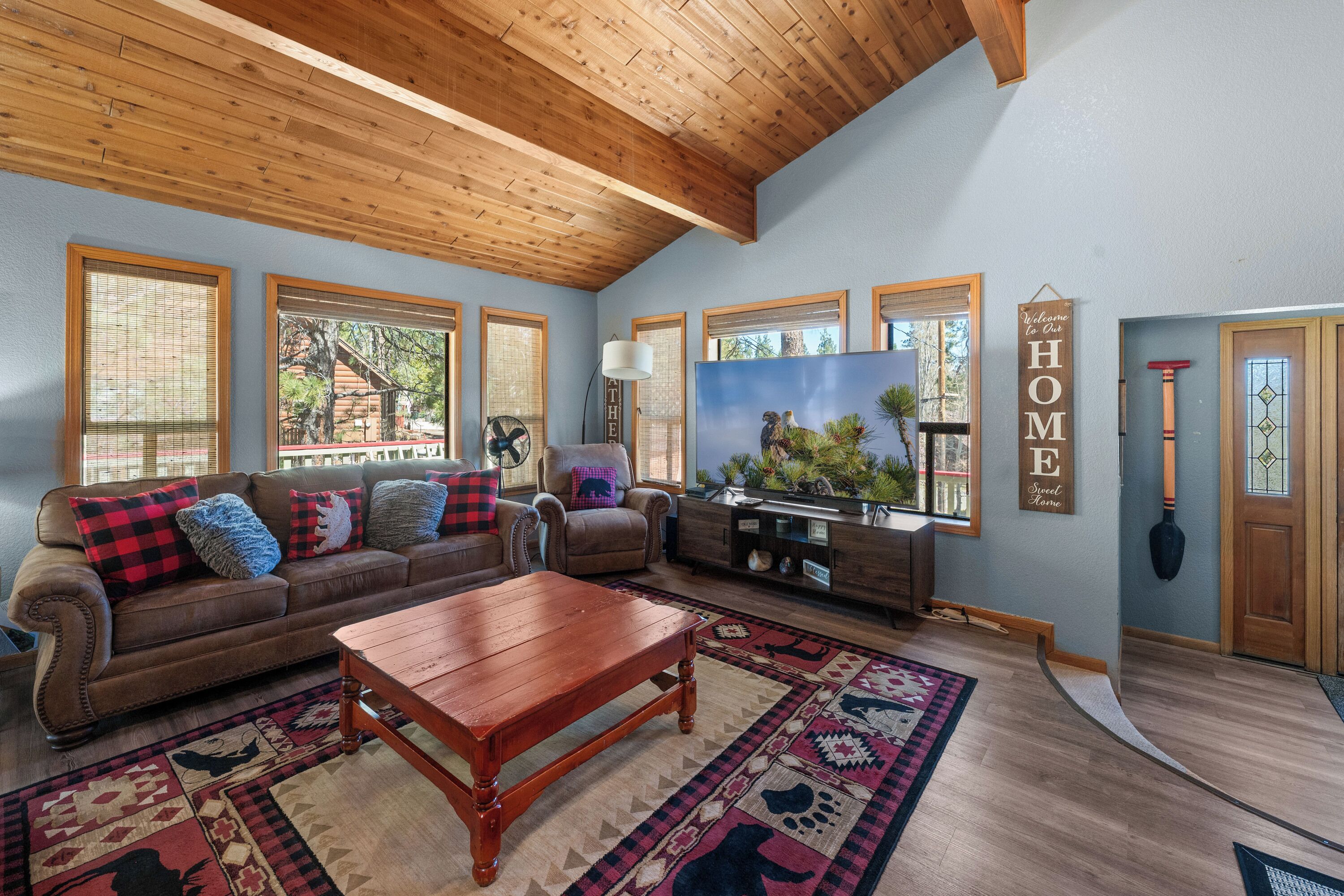 A living room with a wooden ceiling, a brown leather sofa, a wooden coffee table, and a large flat-screen TV.