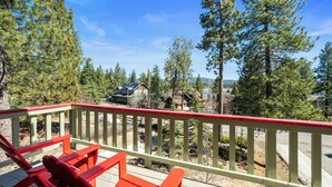 A wooden deck with red chairs, overlooking a forested area with houses and a clear sky. - Lakeview Haven- Luxury Retreat (Big Bear Lake)