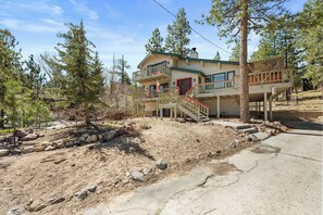 A two-story house with a balcony, a staircase, and a surrounding landscape with trees and rocks. - Lakeview Haven- Luxury Retreat (Big Bear Lake)