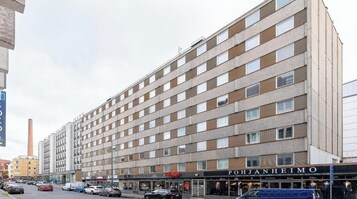 Un hotel de varios pisos con una fila de ventanas en cada planta, una tienda con un letrero y un estacionamiento lleno de coches.