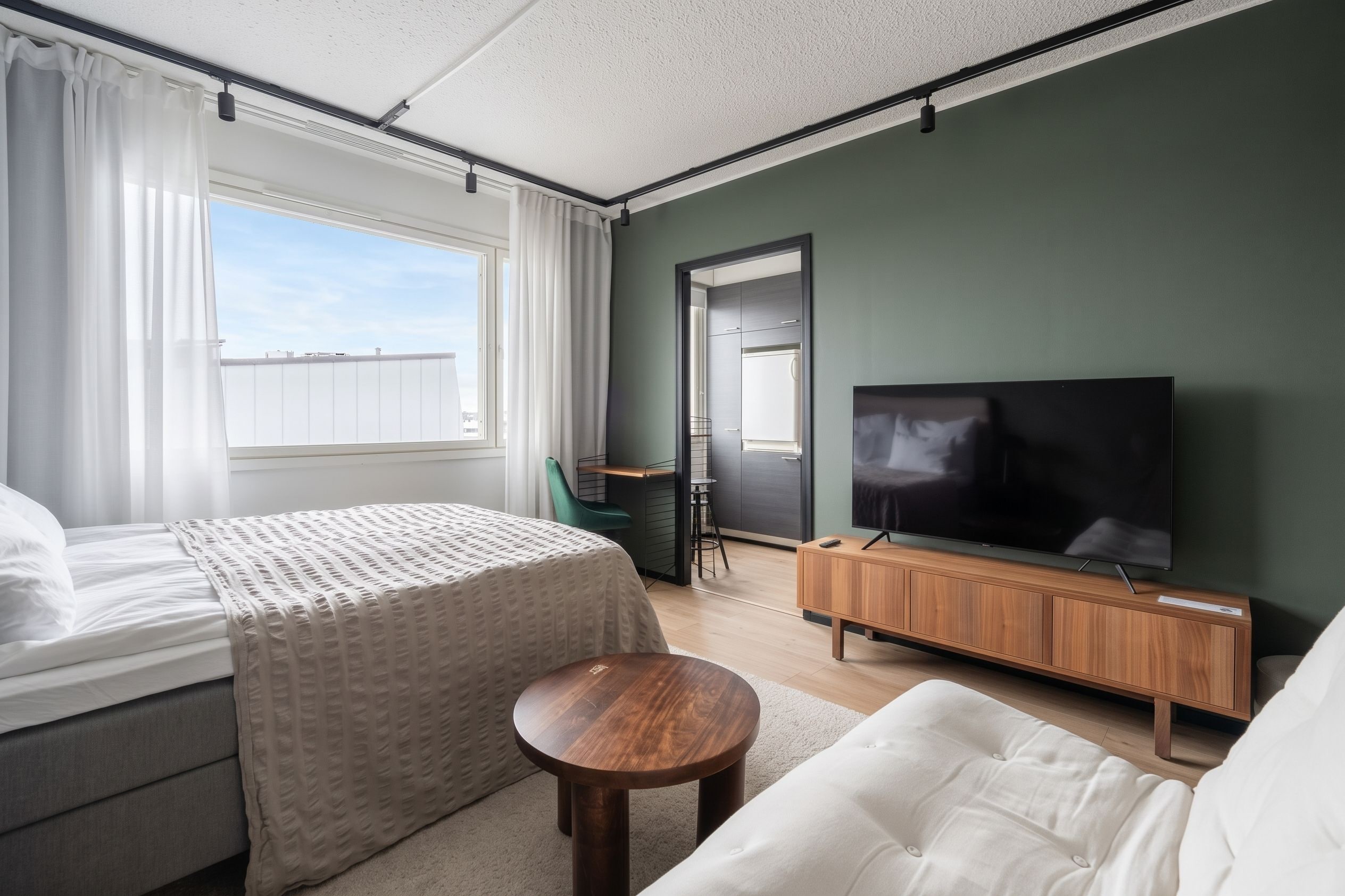 Habitació d'hotel moderna amb llit, sofà, televisió i taula petita.