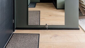 Een kamer met een donkergroene wand, een houten vloer, een zwarte deur en een klein raam.
