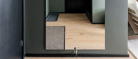 A room with a dark green wall, a wooden floor, a black door, and a small window.