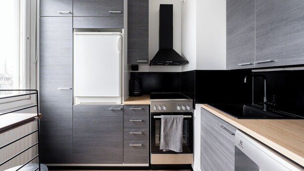 Een moderne keuken met grijze kastjes, een ingebouwde oven en een zwarte afzuigkap.