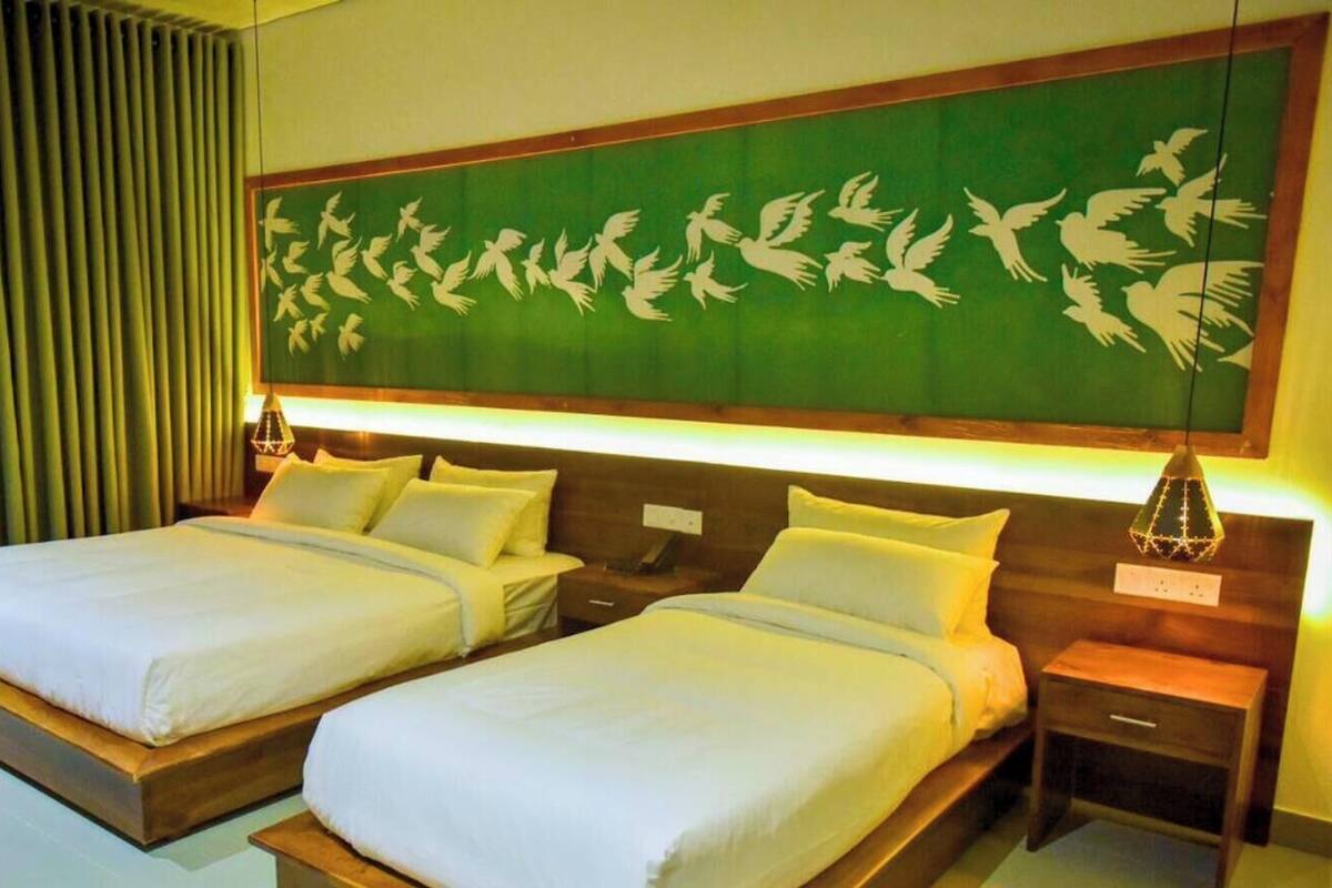 Une chambre d’hôtel avec deux lits, un mur vert orné d’une fresque représentant un oiseau blanc et une tête de lit en bois.