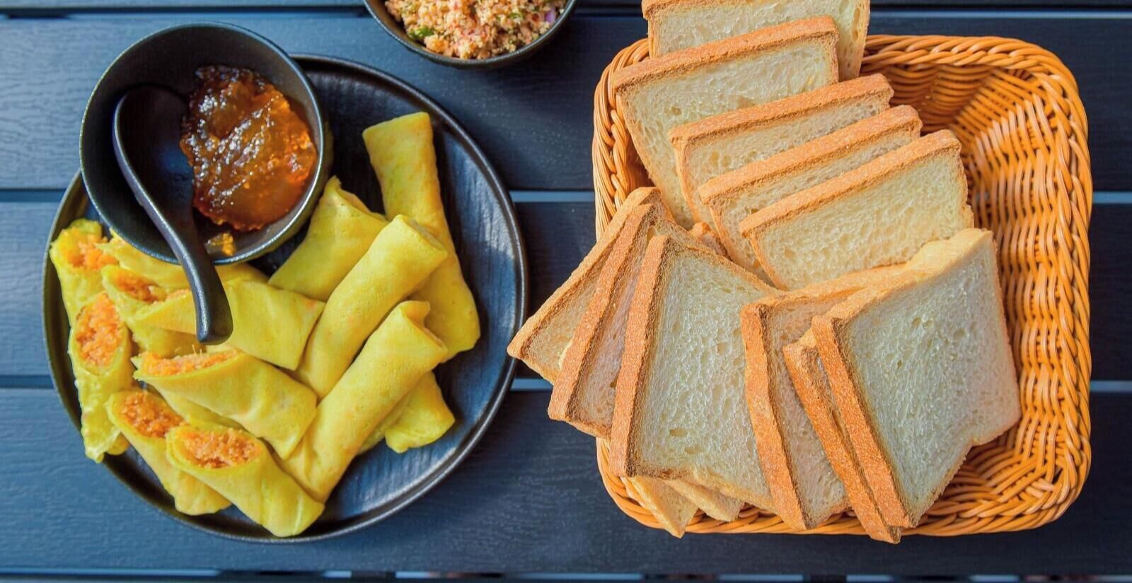 A basket of sliced bread and a plate of spring rolls with dipping sauce.