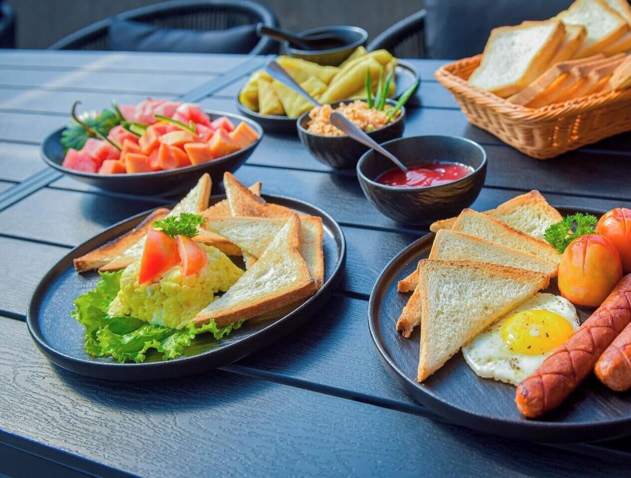 Une table garnie de divers aliments pour le petit-déjeuner, notamment des toasts, des œufs, des saucisses et des fruits.
