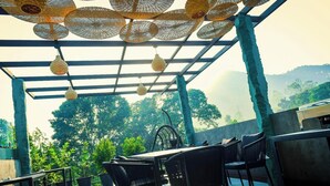 Un espacio de estar techado al aire libre con mobiliario de mimbre y lámparas colgantes.