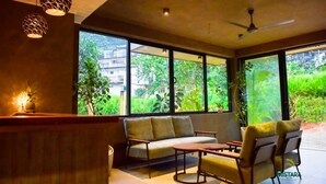 Un interior moderno con sofá, sillas, una mesa y ventanas amplias que dan a zonas verdes y edificios.