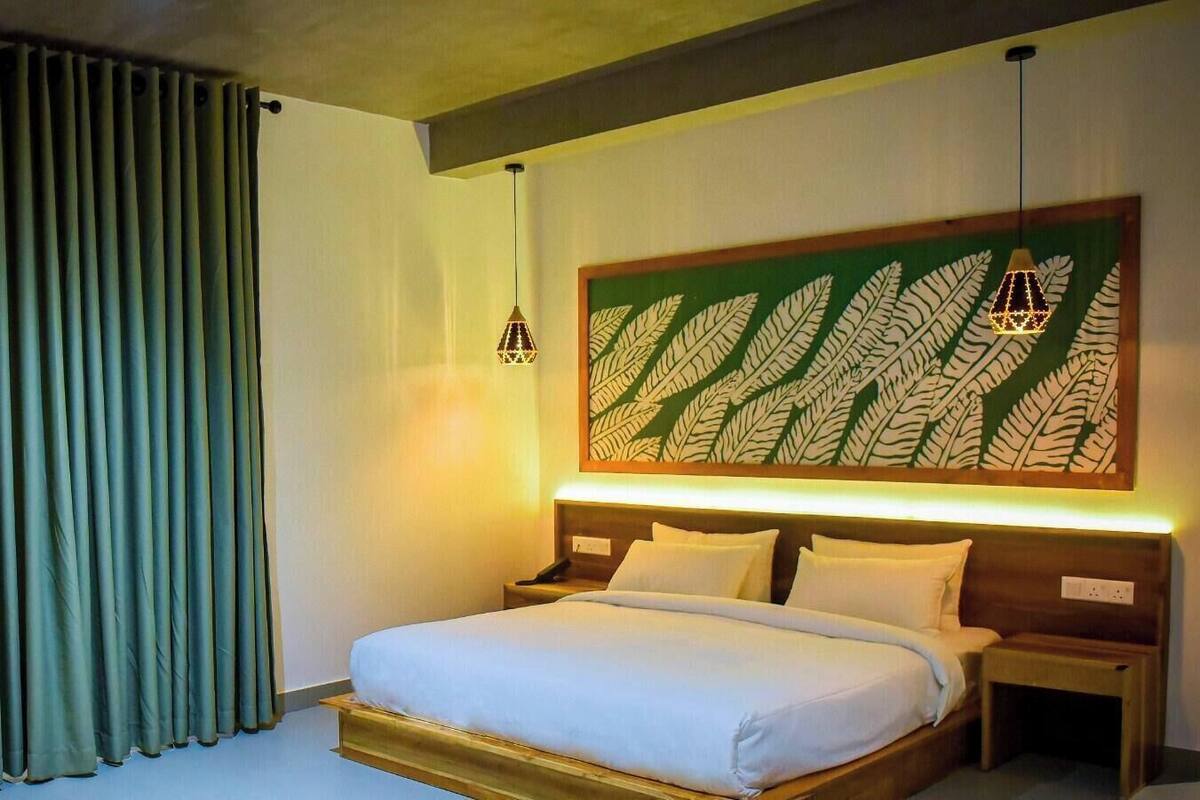 Une chambre d’hôtel avec un lit, des tables de chevet, une grande décoration murale représentant une fougère et un rideau.