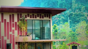 Un edificio moderno con balcón, ventanas amplias y vistas a una ladera boscosa.
