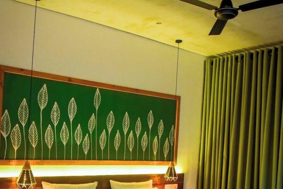 Une chambre d’hôtel avec un lit, un ventilateur de plafond, une décoration murale à motifs de feuilles vertes et une fenêtre avec des rideaux.