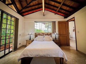 A bedroom with a large bed, two bedside tables, a window, and a wooden ceiling.