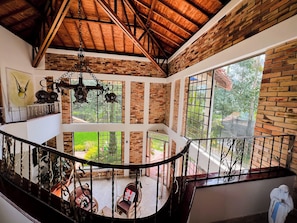 A multi-level interior with exposed brick walls, a wooden ceiling, and a balcony with a view of greenery.